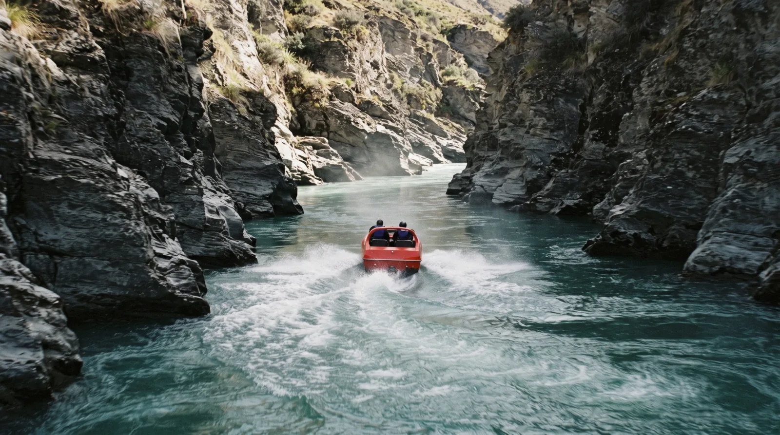A jet boat throwing spray in a narrow schist canyon on the Shotover, one of the Queenstown adventure activities New Zealand is known for