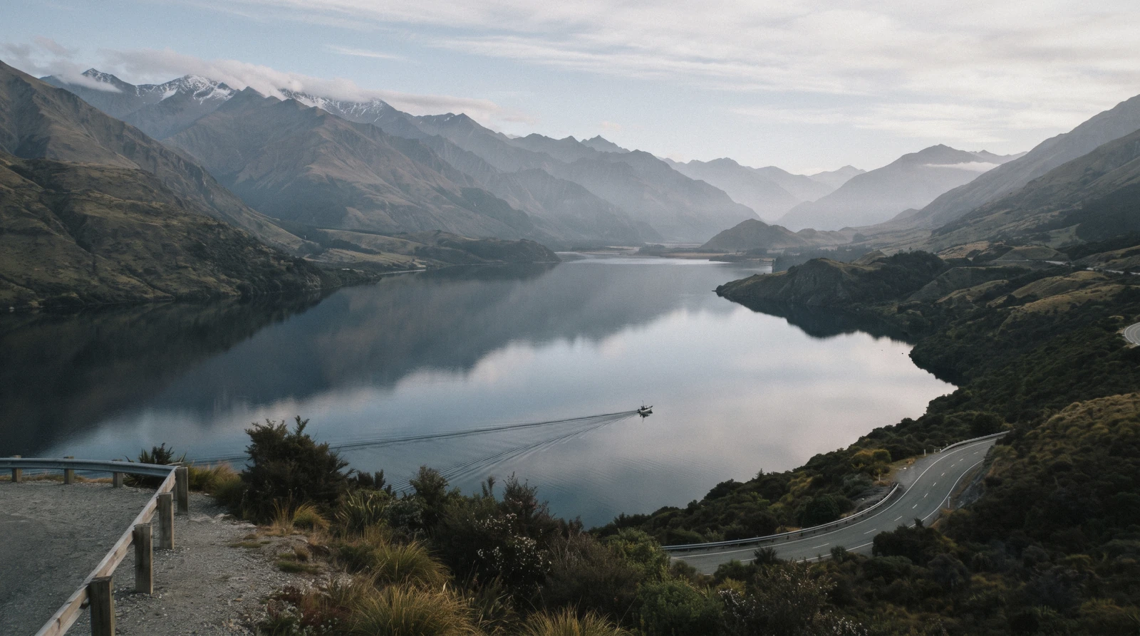 Deep blue water running between steep tussock mountains under low cloud on Lake Wakatipu, Queenstown, New Zealand