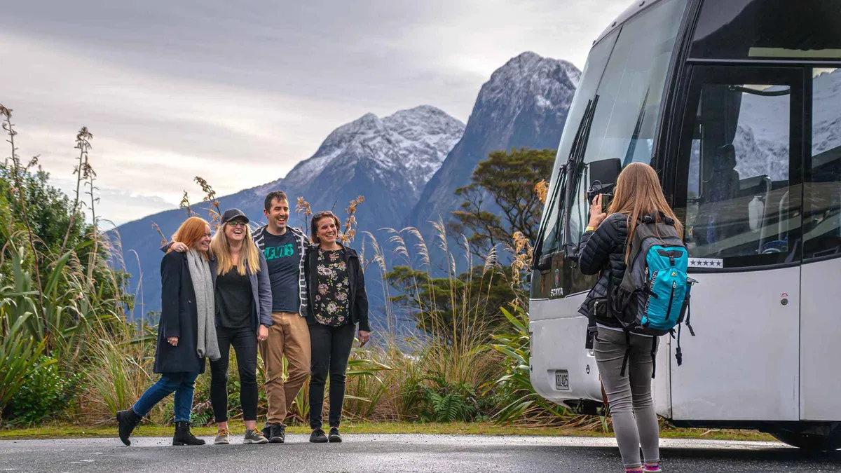 A cruise boat dwarfed by cliffs and waterfalls in Milford Sound — Milford Sound day trip from Queenstown, New Zealand