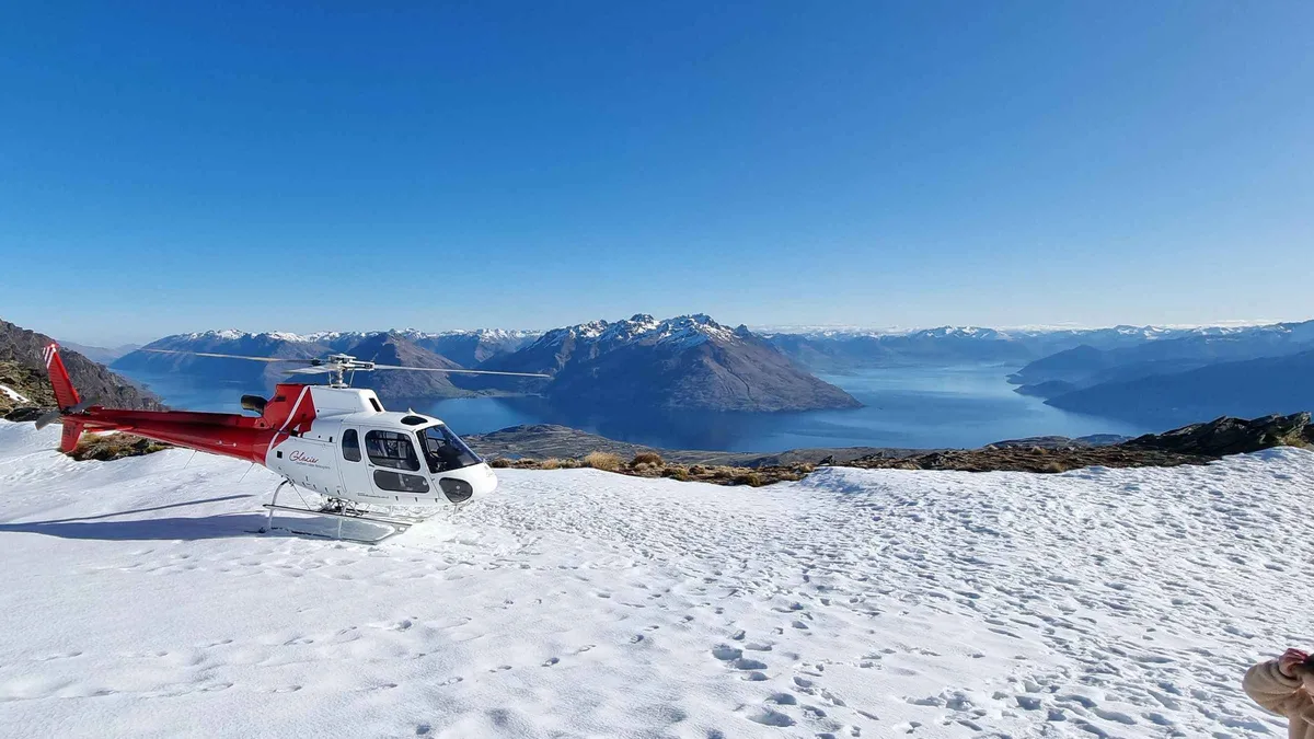 A helicopter parked on a rocky alpine spur above the lake — Queenstown tours, New Zealand